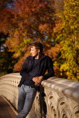 Sonbaharda New York Manhattan Central Park, göl üzerinde köprü. Genç bir adam New York 'ta bir sonbahar parkında yürüyor..