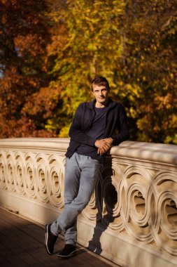 Sonbaharda New York Manhattan Central Park, göl üzerinde köprü. Genç bir adam New York 'ta bir sonbahar parkında yürüyor..