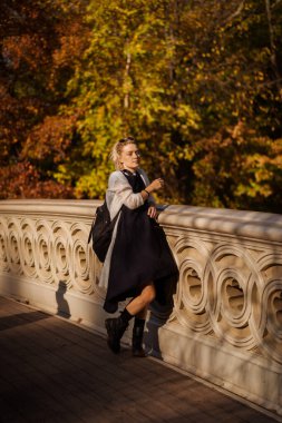 Sonbaharda New York Manhattan Central Park, göl üzerinde köprü. Genç bir kadın New York 'ta bir sonbahar parkında yürüyor..