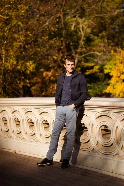 Sonbaharda New York Manhattan Central Park, göl üzerinde köprü. Genç bir adam New York 'ta bir sonbahar parkında yürüyor..