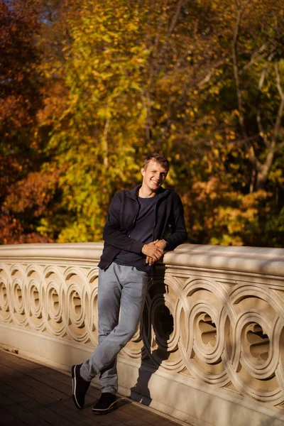 Sonbaharda New York Manhattan Central Park, göl üzerinde köprü. Genç bir adam New York 'ta bir sonbahar parkında yürüyor..