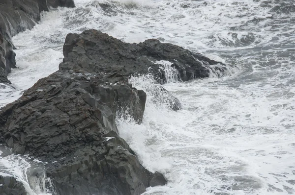 Деталь волн на пляже из черного песка с камнями — стоковое фото