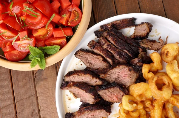 Bife flanco com batatas fritas anéis de cebola e salada — Fotografia de Stock