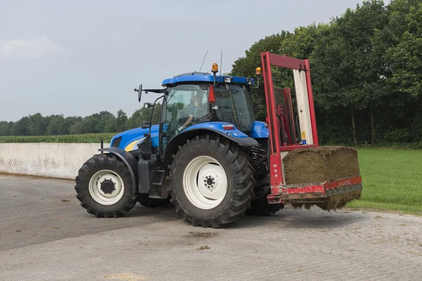 Tractor azul con una rebanadora de pacas roja — Foto de Stock