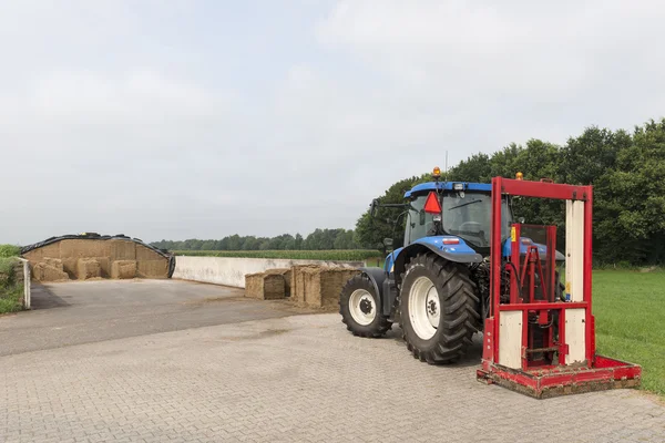 Tractor azul con una rebanadora de pacas roja — Foto de Stock