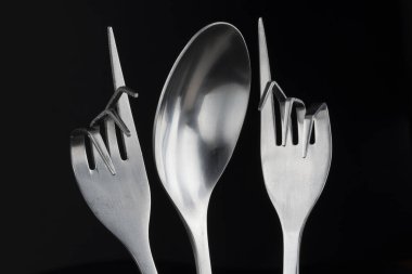 Paslanmaz çelik kaşığın kavramsal figürü ve siyah arka planda iki paslanmaz çelik çatal.