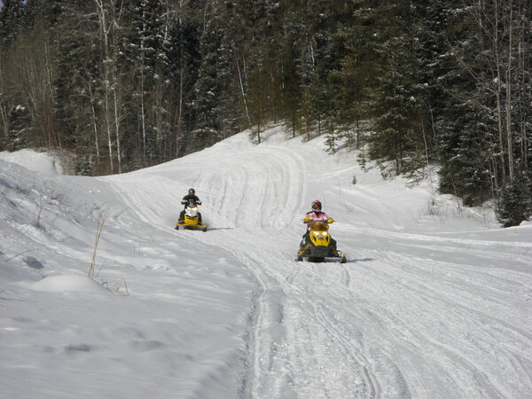 Two snowmobilers riding on a groomed snowmobile trail near Waskesiu in Central Saskatchewan.