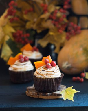 Ev yapımı balkabaklı kekler kremalı kekler, böğürtlenler ve balkabağı parçaları arka planda sonbahar yaprakları olan siyah ahşap masa üzerinde. Seçici odak