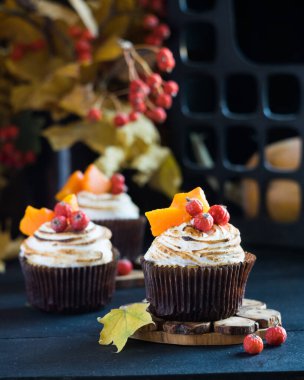 Ev yapımı balkabaklı kekler kremalı kekler, böğürtlenler ve balkabağı parçaları arka planda sonbahar yaprakları olan siyah ahşap masa üzerinde. Seçici odak