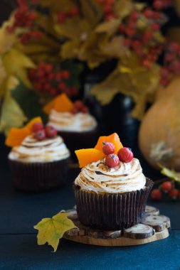 Ev yapımı balkabaklı kekler kremalı kekler, böğürtlenler ve balkabağı parçaları arka planda sonbahar yaprakları olan siyah ahşap masa üzerinde. Seçici odak