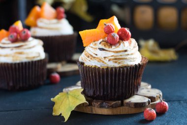 Ev yapımı balkabaklı kekler, kremalı kekler, böğürtlenler ve siyah ahşap masada duran balkabağı parçaları. Seçici odak, yakın plan