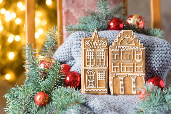 Örgü bir süveterin üzerinde iki zencefilli kek evi ve arka planda Noel süslemeleri. Seçici odak.
