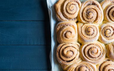 Taze pişmiş tarçınlı çörekler parşömen kağıdının üzerinde tarçınlı çörekler ve siyah ahşap masa. Üst görünüm, telif alanı. Ev yapımı tatlı hamur işi Noel pastası..
