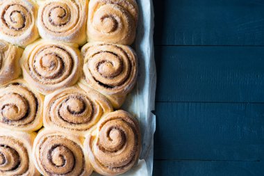 Taze pişmiş tarçınlı çörekler parşömen kağıdının üzerinde tarçınlı çörekler ve siyah ahşap masa. Üst görünüm, telif alanı. Ev yapımı tatlı hamur işi Noel pastası..