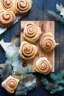 Taze pişmiş tarçınlı çörekler parşömen kağıdının üzerinde tarçınlı çörekler köknar ağacı dalları, tarçın ve anason yıldızları olan siyah ahşap masa. Üst Manzara. Ev yapımı tatlı hamur işi Noel pastası..