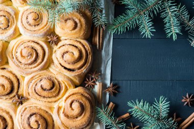 Taze pişmiş tarçınlı çörekler parşömen kağıdının üzerinde tarçınlı çörekler köknar ağacı dalları, tarçın ve anason yıldızları olan siyah ahşap masa. Üst görünüm, telif alanı. Ev yapımı tatlı hamur işi Noel pastası..