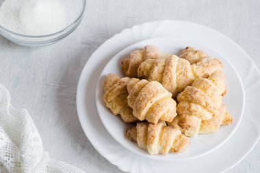 Ev yapımı süzme peynirli çörekler simit rogaliki üzerine beyaz tabakta şeker, gri arka plan, seçici odak