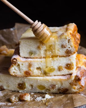 Ahşap bir masadaki kabartma kağıdının üzerinde kuru üzüm ve bal olan süzme peynir güvecine yakın çekim. Geleneksel Rus tatlı zapekankası