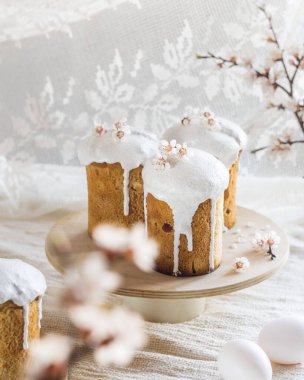 Geleneksel Paskalya ekmeği ya da pasta, beyaz kremayla süslenmiş ve keten masa örtüsü üzerine çiçekler, seçici odaklanma, dikey yönelim. Paskalya konsepti.