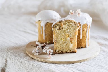 Geleneksel Paskalya ekmeği ya da pasta, beyaz kremayla süslenmiş ve keten masa örtüsü üzerine çiçekler, seçici odak, yatay yönelim. Paskalya konsepti.