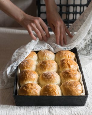 Ev yapımı ekmek ruloları, keten masa örtüsünün üzerinde teneke kalıplar, arka planda kadın elleri. Seçici odaklanma, dikey yönelim