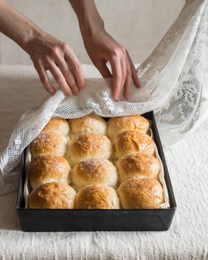 Ev yapımı ekmek ruloları, keten masa örtüsünün üzerinde teneke kalıplar, arka planda kadın elleri. Seçici odaklanma, dikey yönelim