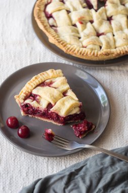 Açık keten arka planda gri tabakta çatalı olan bir parça vişneli pasta, seçici odaklı.