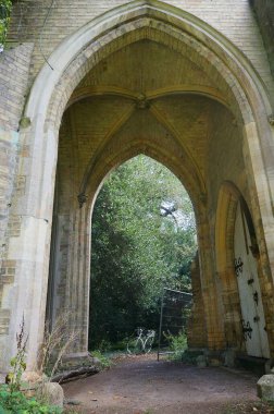 Arka planda bisikletle eski mezarlıktaki bir ortaçağ şapelinin kemerli yoluna giden yol.