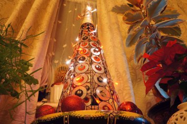 Evin her iki tarafında da ev bitkileri olan büyüleyici yapay Noel ağacı var.