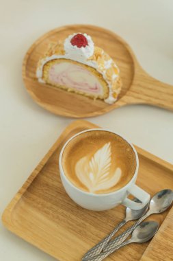 Bir fincan kapuçino ve bir dilim kekle ahşap masa manzarası.