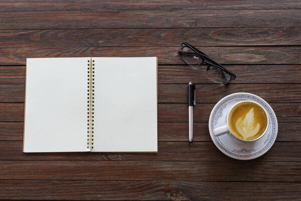 Top view of desk table with a pen, glasses, note, and cup of cappuccino