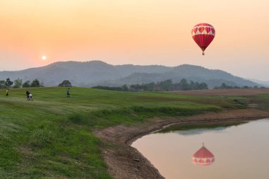 Renkli aerostat balonunun fotoğrafı. Arkasında güzel bir manzarayla gölün üstünde havada yüzen sepet.
