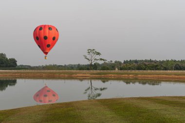 Renkli aerostat balonunun fotoğrafı. Arkasında güzel bir manzarayla gölün üstünde havada yüzen sepet.