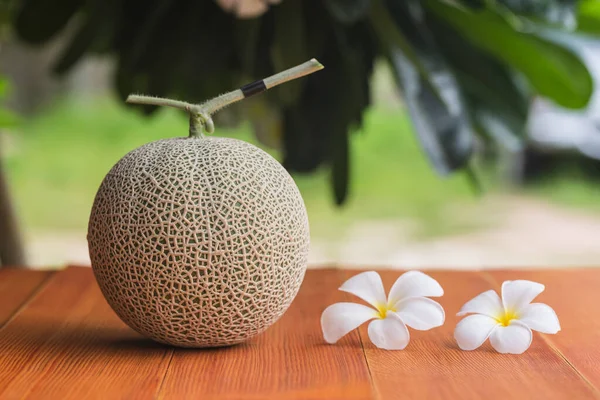 Ahşap masadaki kavun fotoğrafında yapraklar ve arka planda alçak.