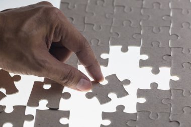 Adamın eli yapbozun bir parçasını beyaz arka plana yerleştirmeye çalışıyor.