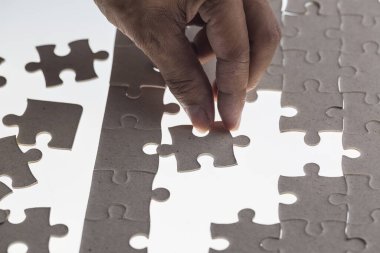 Adamın eli yapbozun bir parçasını beyaz arka plana yerleştirmeye çalışıyor.