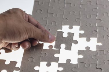 Adamın eli yapbozun bir parçasını beyaz arka plana yerleştirmeye çalışıyor.