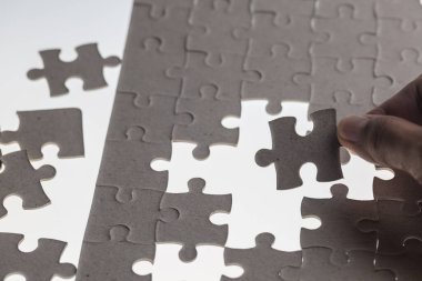 Adamın eli yapbozun bir parçasını beyaz arka plana yerleştirmeye çalışıyor.