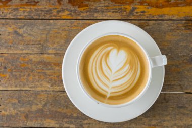 Latte sanat eseri, sıcak kahve fincanı ahşap masada. 