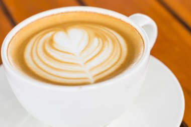 Latte sanat eseri, sıcak kahve fincanı ahşap masada. 