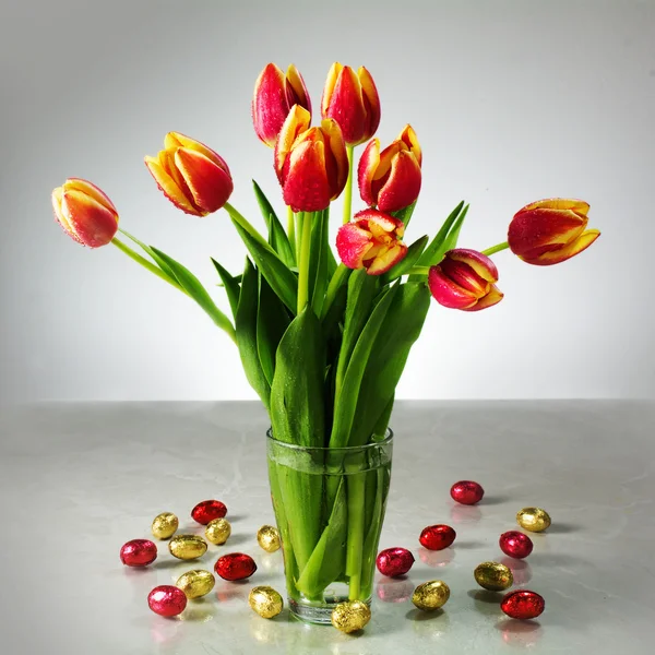 Bouquet of fresh tulips and small red yellow chocolate easter eg — 스톡 사진