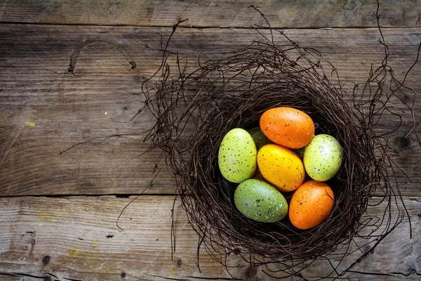 Uova di Pasqua verdi e arancioni in un nido su tavole di legno rustiche w — Foto Stock