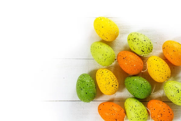 Easter eggs in green, yellow and orange on white wood, corner ba — Stock Photo, Image