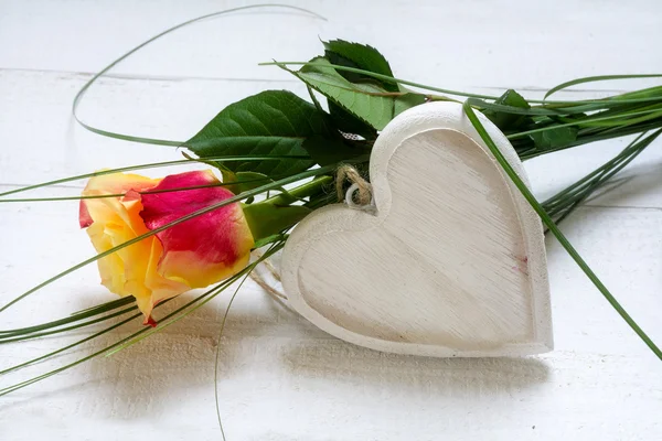 Rosa e um coração de madeira em branco em madeira pintada de branco, conceito para o amor — Fotografia de Stock