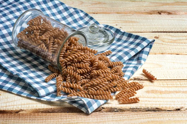 Volkoren deegwaren uit een glazen pot op een blauwe gedessineerde keuken handdoek — Stockfoto