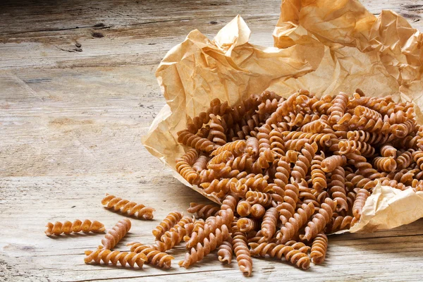 Wholemeal pasta fusilli from organic whole grain spelt falling from a paper bag — Stock Photo, Image