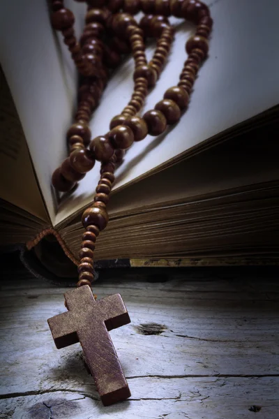 Cuentas de rosario de madera con cruz en un viejo libro sobre madera rústica, símbolo religioso —  Fotos de Stock