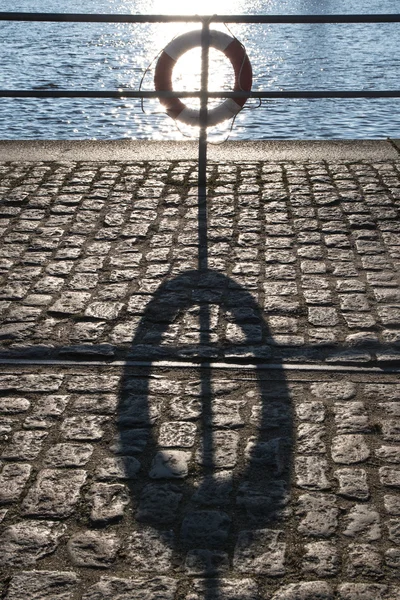 Lifebuoy in the back light on the railing and a long shadow on the pier — Stock Photo, Image