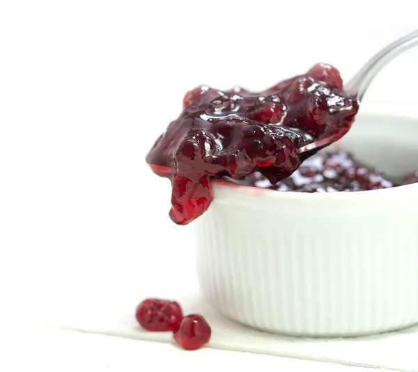 Rote Preiselbeermarmelade, die von einem Löffel über eine kleine Schüssel tropft, Nahaufnahme auf weiß — Stockfoto