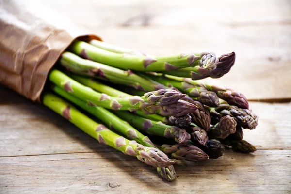 Green asparagus bunch in brown paper on a rustic wooden board — Stock Photo, Image